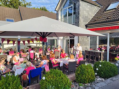 Dame mit Mikrofon unter Sonnenschirm mit vielen weiteren Zuhörerinnen.